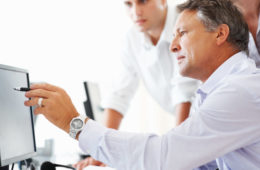 Mature business man discussing project with his colleagues and pointing at computer screen
